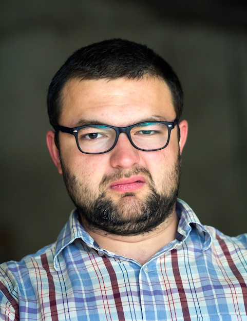 Portrait of handsome bearded black haired intelligent modern young man in glasses with short haircut and kind black eyes smiling in camera