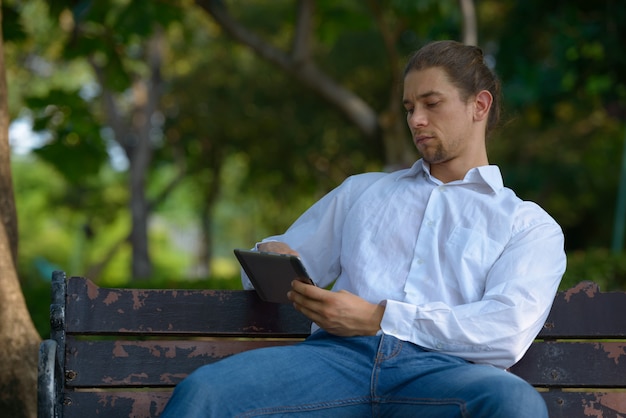 Portrait of handsome bearded businessman with long hair relaxing at the park outdoors