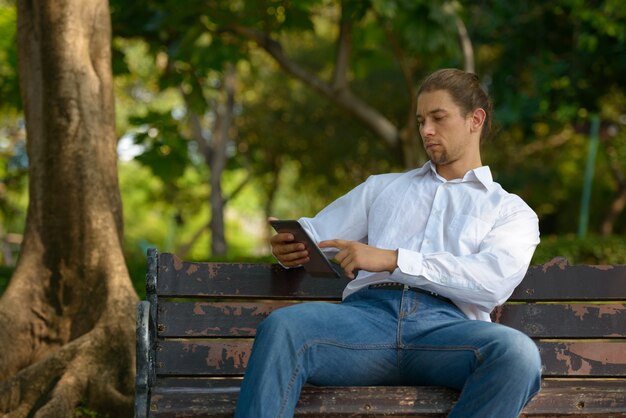 Portrait of handsome bearded businessman with long hair relaxing at the park outdoors