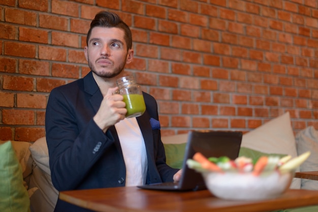 Portrait of handsome bearded Hispanic businessman relaxing at the coffee shop