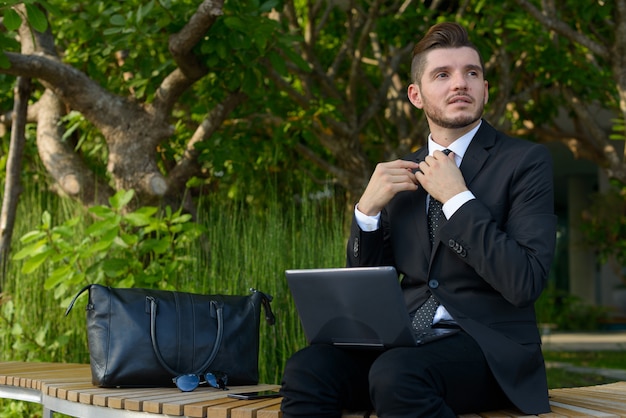 Portrait of handsome bearded Hispanic businessman with nature in the city outdoors