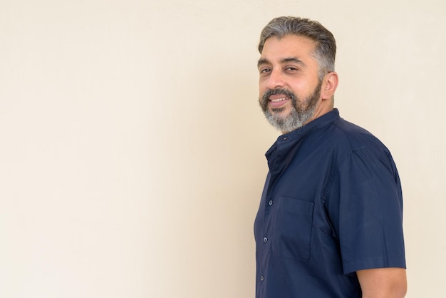 Portrait of handsome bearded Indian businessman against plain background