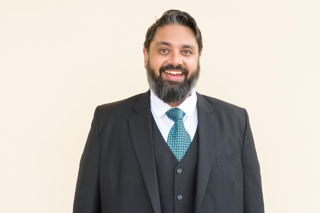 Portrait of handsome bearded Indian businessman smiling against plain background