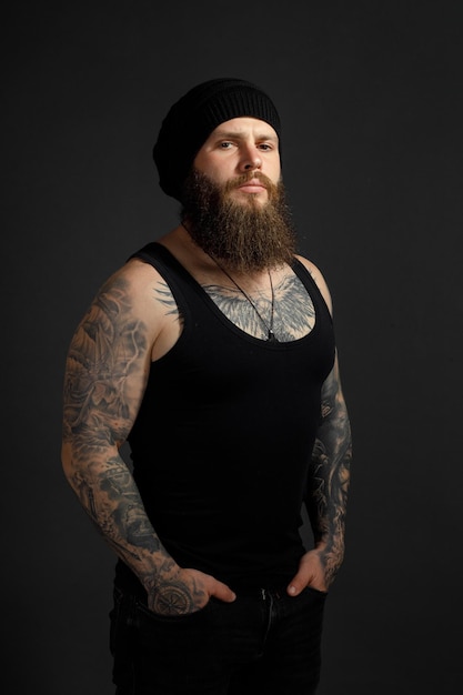 Portrait of a handsome bearded man in a black t-shirt and hat looking at the camera.