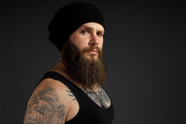 Portrait of a handsome bearded man in a black t-shirt and hat looking at the camera.