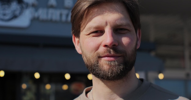 Portrait of handsome bearded man holding cup of takeout coffee and smiling standing on street on nice day drinking coffee