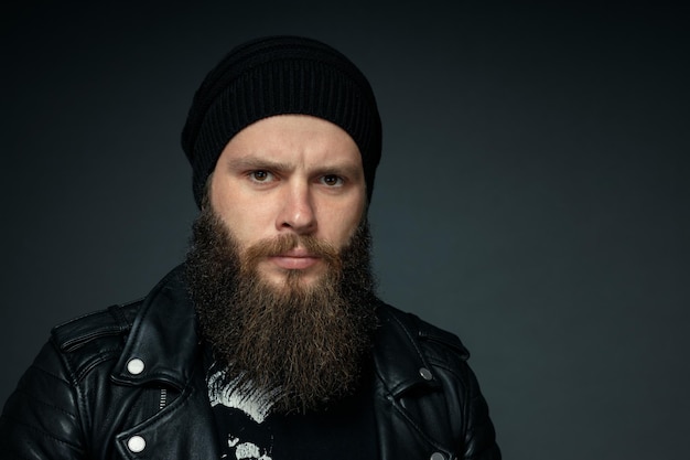 Portrait of handsome bearded man in leather jacket and hat looking at the camera