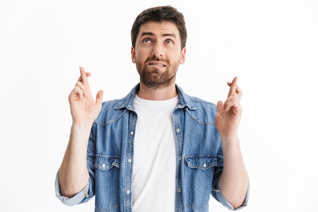 Portrait of a handsome bearded man wearing casual clothes standing isolated, holding fingers crossed for good luck