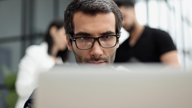 Portrait of handsome bearded man wearing glasses working with laptop in office late his face lit up by screen