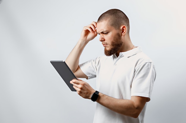 Portrait of a handsome bearded man in a white t-shirt working in a tablet