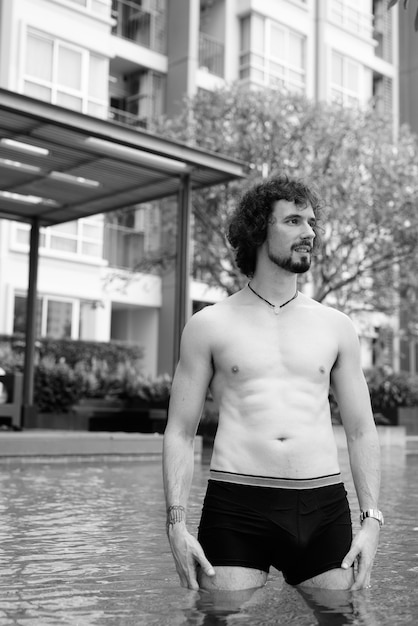 Portrait of handsome bearded man with curly hair shirtless relaxing beside the swimming pool