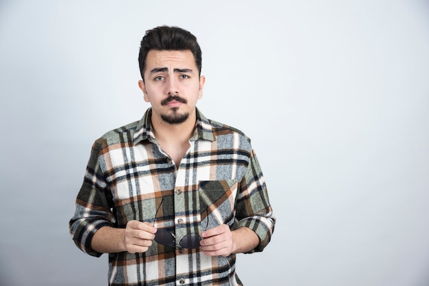 Portrait of handsome bearded man with glasses posing and standing over white wall.