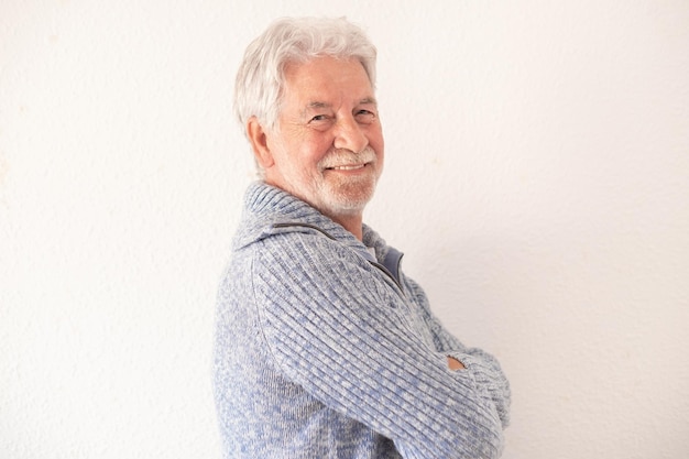 Portrait of handsome bearded senior man in casual clothes with crossed arms smiling and looking at the camera while standing on white background