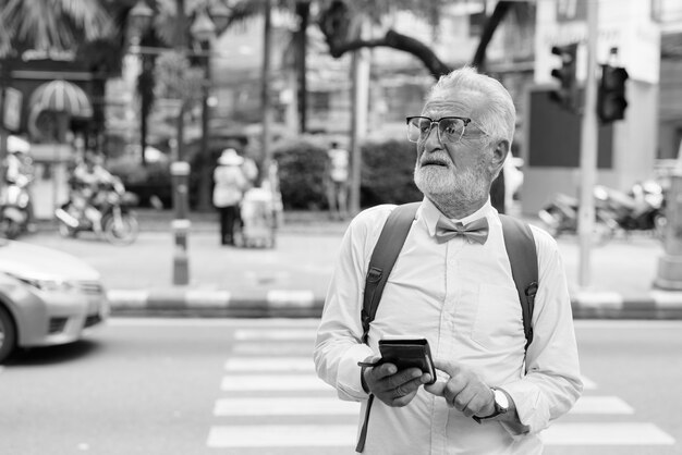 Portrait of handsome bearded senior tourist man wearing stylish clothes while exploring the city of Bangkok in black and white