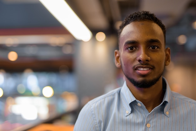 Portrait of handsome black African businessman face looking at camera inside shopping mall