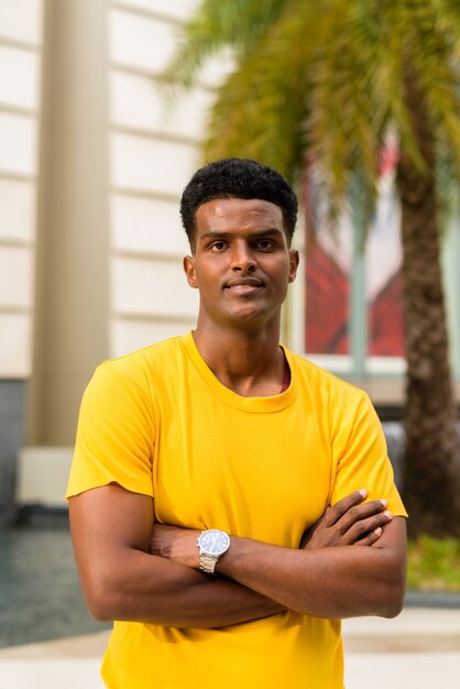 Portrait of handsome black African man wearing yellow t-shirt outdoors in city during summer with arms crossed