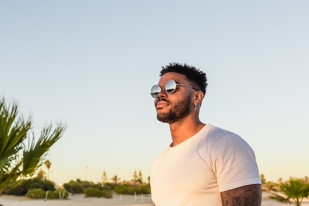 Foto ritratto di un bell'uomo nero americano che indossa occhiali da sole durante il tramonto in spiaggia