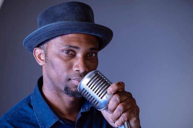 Portrait of handsome black man about to sing a vintage song. Isolated male singing ethnic cultural songs. Young african american singer holding trendy microphone