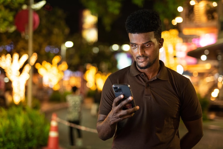 Portrait of handsome black man in city at night using phone