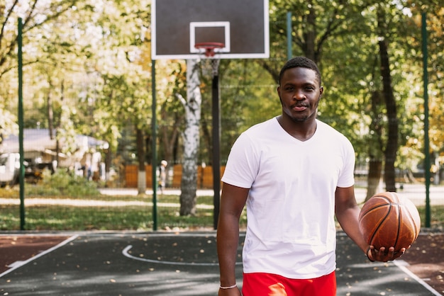 농구 코트에서 농구를 들고 있는 잘생긴 흑인 청년의 초상화. 운동 중에는 휴식을 취하십시오. 유행 스포츠 초상화입니다.