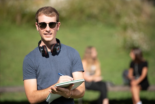 Portrait of a handsome blond boy wearing sunglasses and writing on a notebook