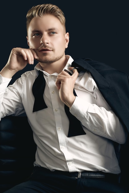 Photo portrait of handsome blond man in elegant tuxedo and bow tie posing on black