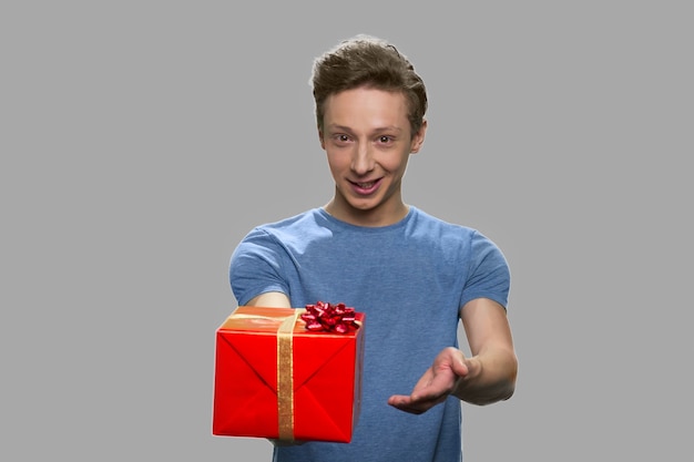 Portrait of handsome boy offering gift box. Cute teen guy holding present box. Special holiday offer.