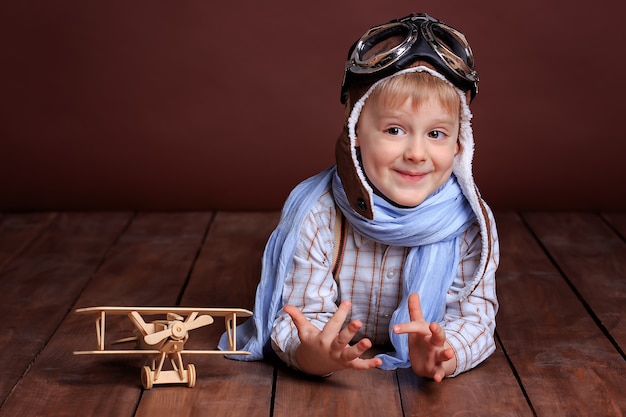 Portrait of a handsome boy in a pilot's helmet and blue scarf with a wooden plane