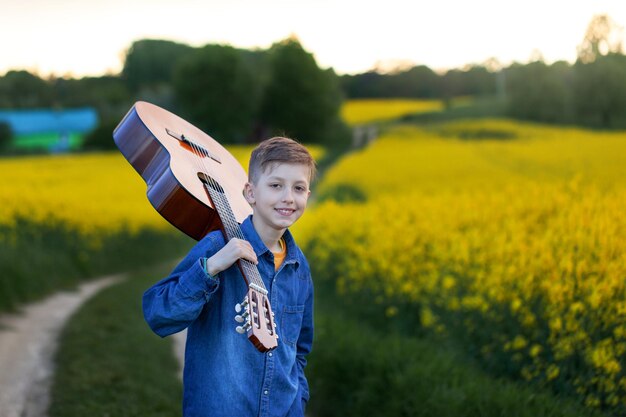 Portrait handsome boy with guitar walking on the summer road. Young musician on the road to success.