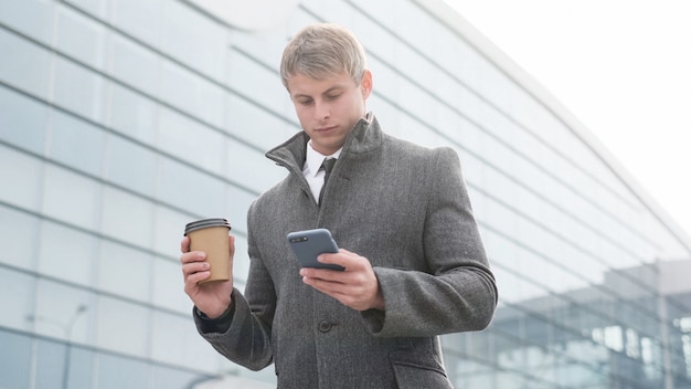 スマートフォンを使用して、街でコーヒーを飲みながらハンサムなビジネスの男の肖像画。