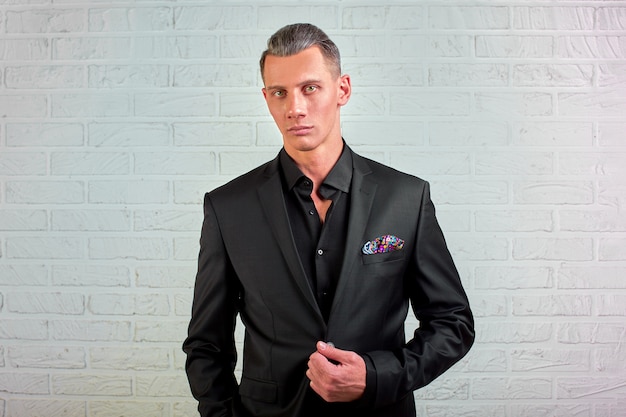 Portrait of handsome businessman in black suit standing on wall wall copy space