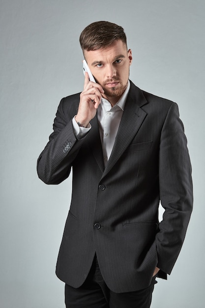 Portrait of a handsome businessman making phone call against grey background