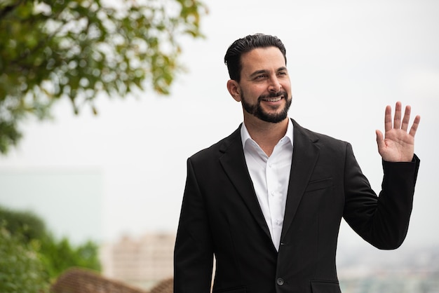 Portrait of handsome businessman outdoors at rooftop waving hand