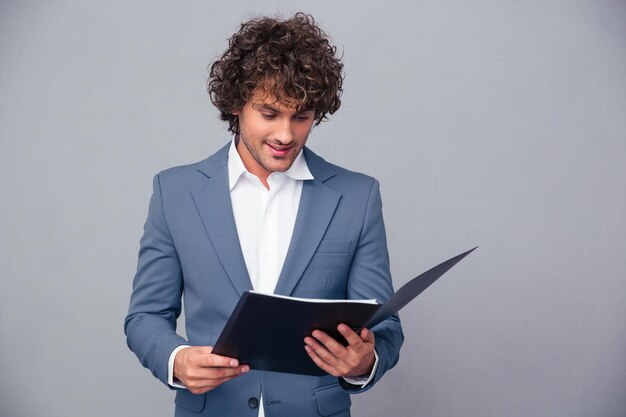 Portrait of a handsome businessman reading documents in folder over gray wall