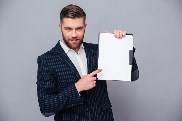 Portrait of a handsome businessman showing blank clipboard over gray wall