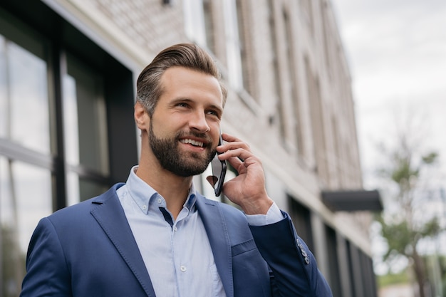 Portrait of handsome businessman wearing stylish suit talking on mobile phone outdoors