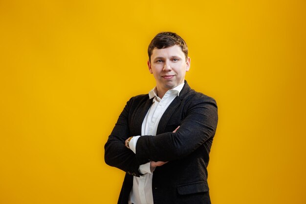 Portrait of handsome businessman with crossing hands standing on yellow studio background and looking at camera