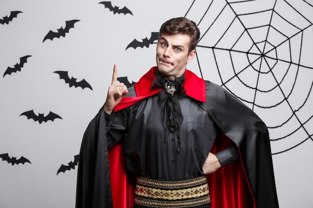 Portrait of handsome caucasian in Vampire halloween costume poining on side. 