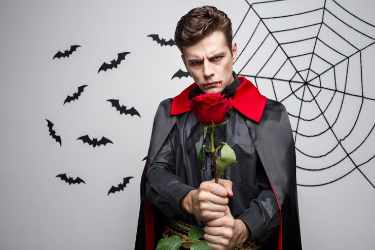 Photo portrait of handsome caucasian vampire holding red beautiful rose. 