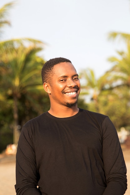 Photo portrait of handsome cheerful african american man in black polo standing with tropical background