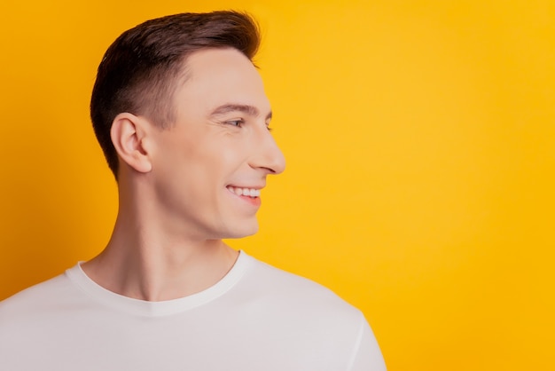 Portrait of handsome cheerful guy look side blank space toothy beaming smile on yellow background