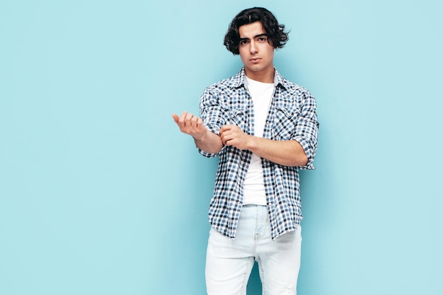 Portrait of handsome confident model sexy stylish man dressed in checkered shirt and jeans fashion hipster male posing near blue wall in studio isolated