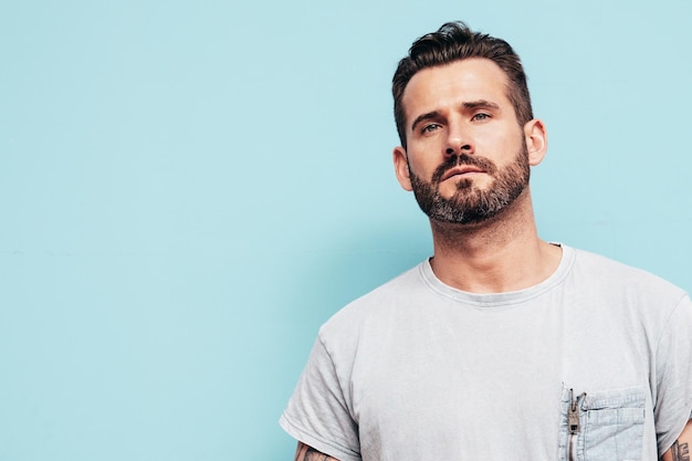 Portrait of handsome confident stylish hipster lambersexual model Sexy man dressed in Tshirt and jeans Fashion male isolated on blue wall in studio