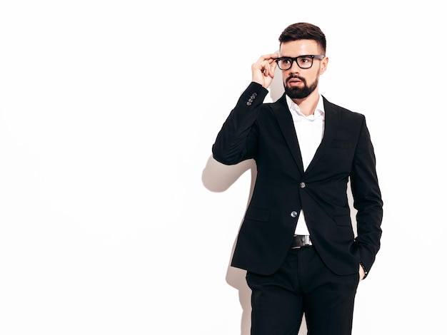 Portrait of handsome confident stylish hipster lambersexual model Sexy modern man dressed in elegant black suit Fashion male posing in studio near white wall Isolated on white In spectacles