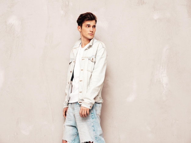 Portrait of handsome confident stylish hipster lambersexual modelMan dressed in jacket and jeans Fashion male posing in studio near grey wall