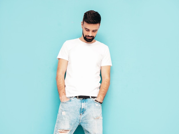 Portrait of handsome confident stylish hipster lambersexual modelMan dressed in white Tshirt and jeans Fashion male isolated on blue wall in studio