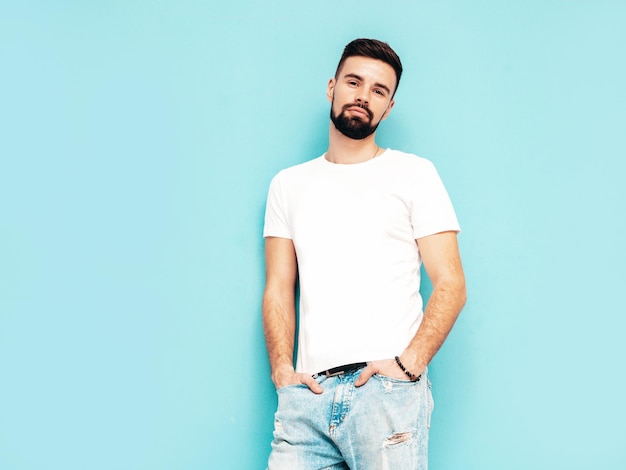 Portrait of handsome confident stylish hipster lambersexual modelMan dressed in white Tshirt and jeans Fashion male isolated on blue wall in studio