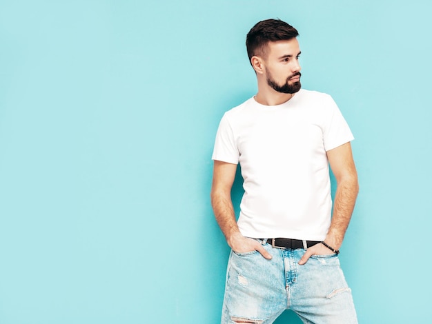 Portrait of handsome confident stylish hipster lambersexual modelMan dressed in white Tshirt and jeans Fashion male isolated on blue wall in studio