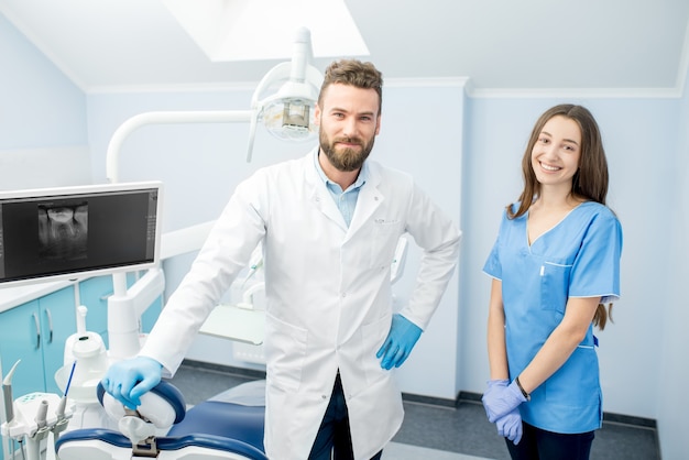 Portrait of handsome dentist with young female assistant in uniform at the dental office