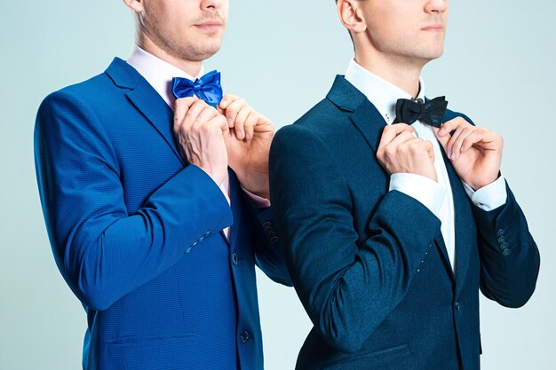 Portrait of handsome and elegant business men wearing bow tie and suits on gray studio background